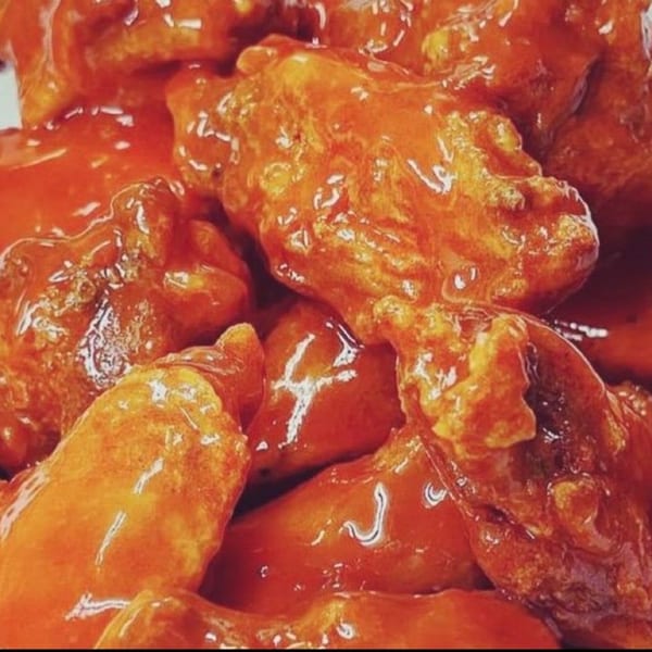 Close-up of DMac & Wings' chicken wings generously coated in a glistening, vibrant orange sauce.