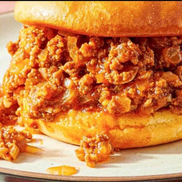 Close-up of a DMac & Wings sloppy joe sandwich with saucy meat and onions spilling out.